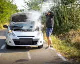 Mężczyzna z rozpaczą w rękach przy białym samochodzie, z którego bucha dym. Rozbiegany diesel na poboczu drogi.