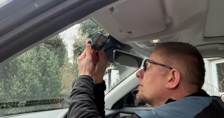 Mężczyzna montuje kamerę samochodową nad lusterkiem wstecznym. Dbałość o szczegóły podczas instalacji zapewnia bezpieczeństwo na drodze.